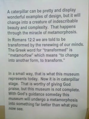 Sign reads: A catepillar can be pretty and display wonderful examples of design, but it will change into a creature of indescribable beauty and complexity. That happens through the miracle of metamorphosis. In Romans 12:2 we are told to be transformed by the renewing of our minds. The Greek word for 'transformed' is 'metamorfow' which means 'to change into another form, to transform.' In a small way, that is what this museum represents today. Now it is in caterpillar stage. That is worthy of giving God praise, but this museum is not complete. With God's guidance someday this museum will undergo a metamorphosis into something far better than what you now see.